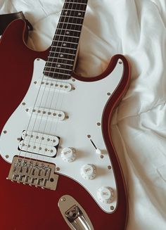 a red electric guitar laying on top of a white sheet with its head resting on it's neck