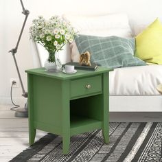 a green end table with flowers on it in front of a white couch and lamp