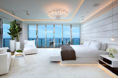 a bedroom with white furniture and large windows overlooking the ocean in front of an open - air balcony