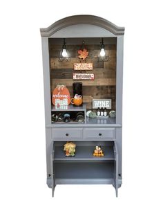 a gray china cabinet with pumpkins and other items on the top, sitting against a white background