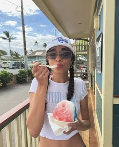 a woman eating an ice cream sundae on the front porch of a building with palm trees in the background