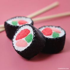 three sushi rolls are sitting on a pink surface with chopsticks in the background