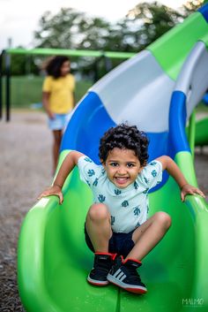 a little boy sitting on top of a green slide