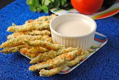 some fried food on a plate next to a bowl of ranch dressing and tomatoes in the background