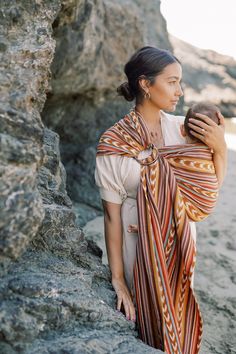 a woman standing on top of a rocky beach next to the ocean holding onto a piece of cloth