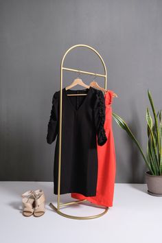 two dresses are hanging on a clothes rack next to a potted plant and shoes