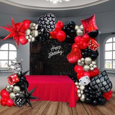 a red table topped with black and white balloons next to a balloon arch that says happy birthday