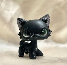 a small black cat with big eyes sitting on a white cloth