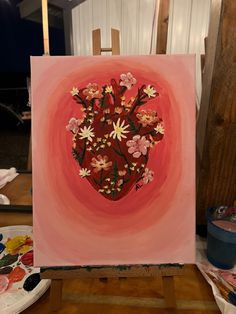 a painting with flowers in the shape of a heart on a easel next to paintbrushes