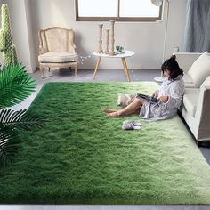 a woman sitting on top of a green rug in a living room next to a couch