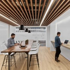 two men working on laptops in an office with wooden ceilinging and white walls