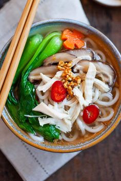 a bowl filled with noodles and vegetables on top of a table next to chopsticks