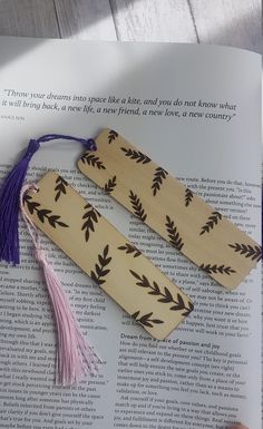 two wooden bookmarks sitting on top of an open book with tassels hanging from them