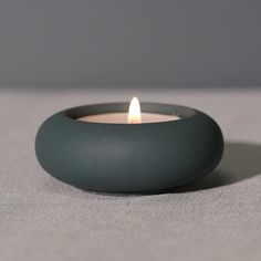 a lit candle sitting on top of a gray table next to a black bowl filled with water