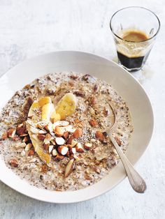 a bowl of oatmeal with bananas and nuts next to a glass of coffee