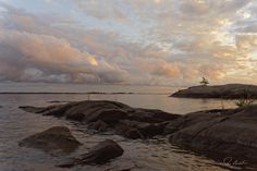 the sky is filled with clouds over some rocks in the water and grass growing on top of them