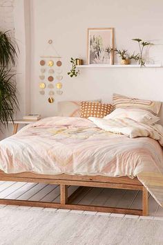 a bed with pillows and blankets in a white room next to a potted plant