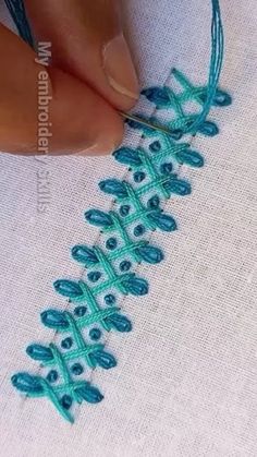 someone is stitching something on a piece of fabric with blue thread and green beads