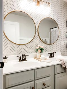 a bathroom with two round mirrors on the wall and white counter tops, along with gray cabinets