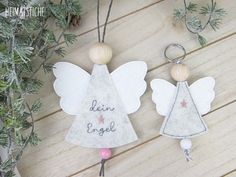 two angel ornaments are hanging on a wooden table next to pine cones and evergreen branches