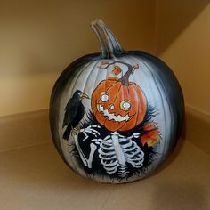 a painted pumpkin with a skeleton and a crow on it's head, sitting on a counter