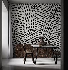 a dining table with two chairs and a vase on it in front of a patterned wall