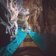 a person in a kayak is paddling through a narrow cave with blue water