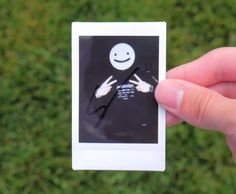 a person holding up a small polaroid with a smiley face on it's side