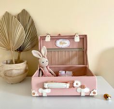 a pink suitcase sitting on top of a white table next to a plant and stuffed animal