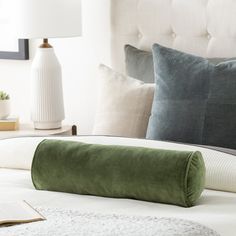 a green pillow on top of a bed next to a white headboard and lamp