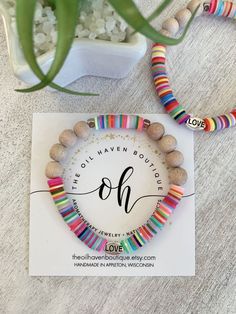 the rainbow beaded bracelets are on display next to a potted plant and card