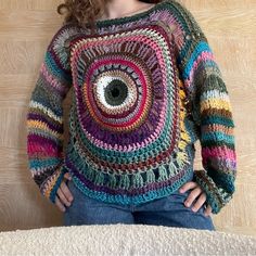 a woman wearing a multicolored crocheted sweater with an eye on it