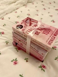 three books are wrapped in pink ribbon on a bed with white sheets and floral print