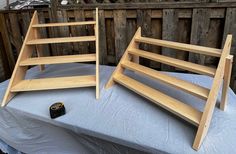 two wooden shelves sitting on top of a blue cloth covered table next to a fence