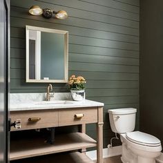 a white toilet sitting next to a sink in a bathroom under a mirror and lights