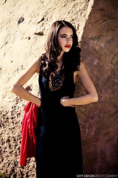 a woman standing in front of a rock wall with her hands on her hips and wearing a black dress