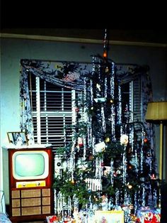 a christmas tree in the corner of a living room with presents on the floor and an old tv