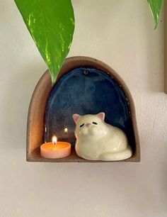 a cat figurine sitting on top of a shelf next to a lit candle