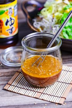 a glass jar filled with liquid sitting on top of a wooden table next to a bowl of salad