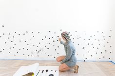 a woman sitting on the floor painting a wall with black polka dot decals and paintbrushes