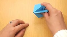 a person is folding an origami piece on top of a wooden table with one hand