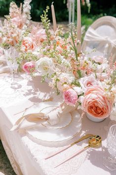 the table is set with pink and white flowers in vases, candles, and napkins