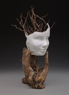 a piece of driftwood with a paper bag on it's head and branches in the background