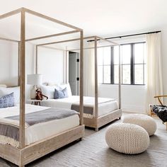 a white bedroom with four poster bed and two stools on the floor next to it