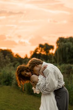 a man and woman kissing each other in front of an orange sky with trees behind them