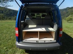 the back end of a blue van with its cargo compartment open in a grassy field