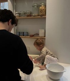 a man standing next to a baby on top of a kitchen counter in front of a bowl