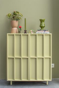 a shelf with books, vases and plants on it in front of a green wall