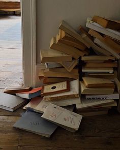 a pile of books sitting on top of a wooden floor next to an open door