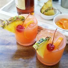 two glasses filled with drinks sitting on top of a wooden table next to bowls of fruit